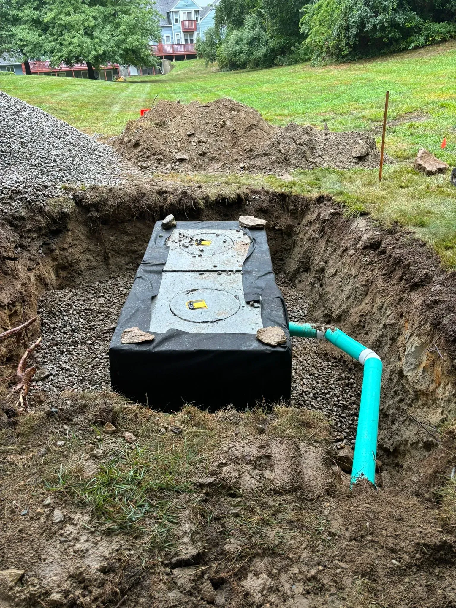Septic tank installed in a dug trench with a blue pipe and dirt piled around it in a yard