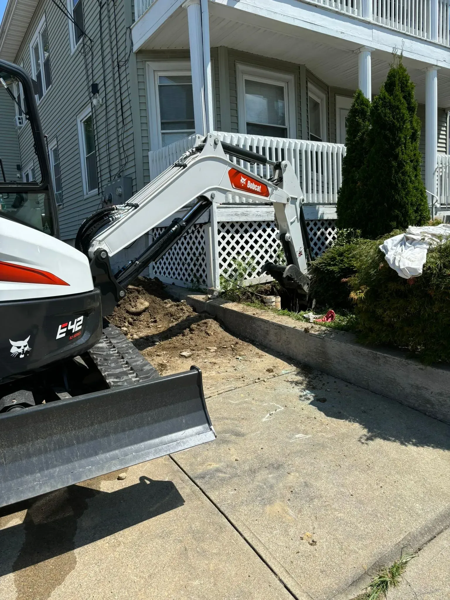 Front porch of a house with white railing, stairs, and a snowplow parked beside a driveway.