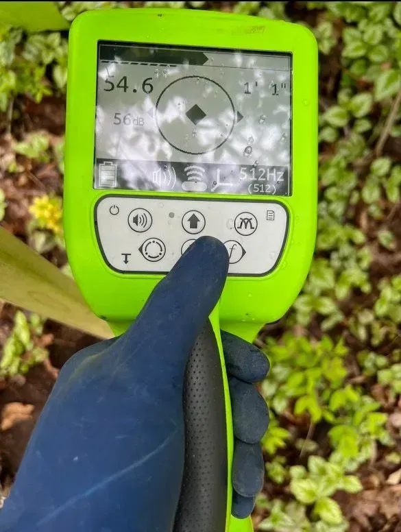 Gloved hand pressing a green handheld meter with a digital display outdoors