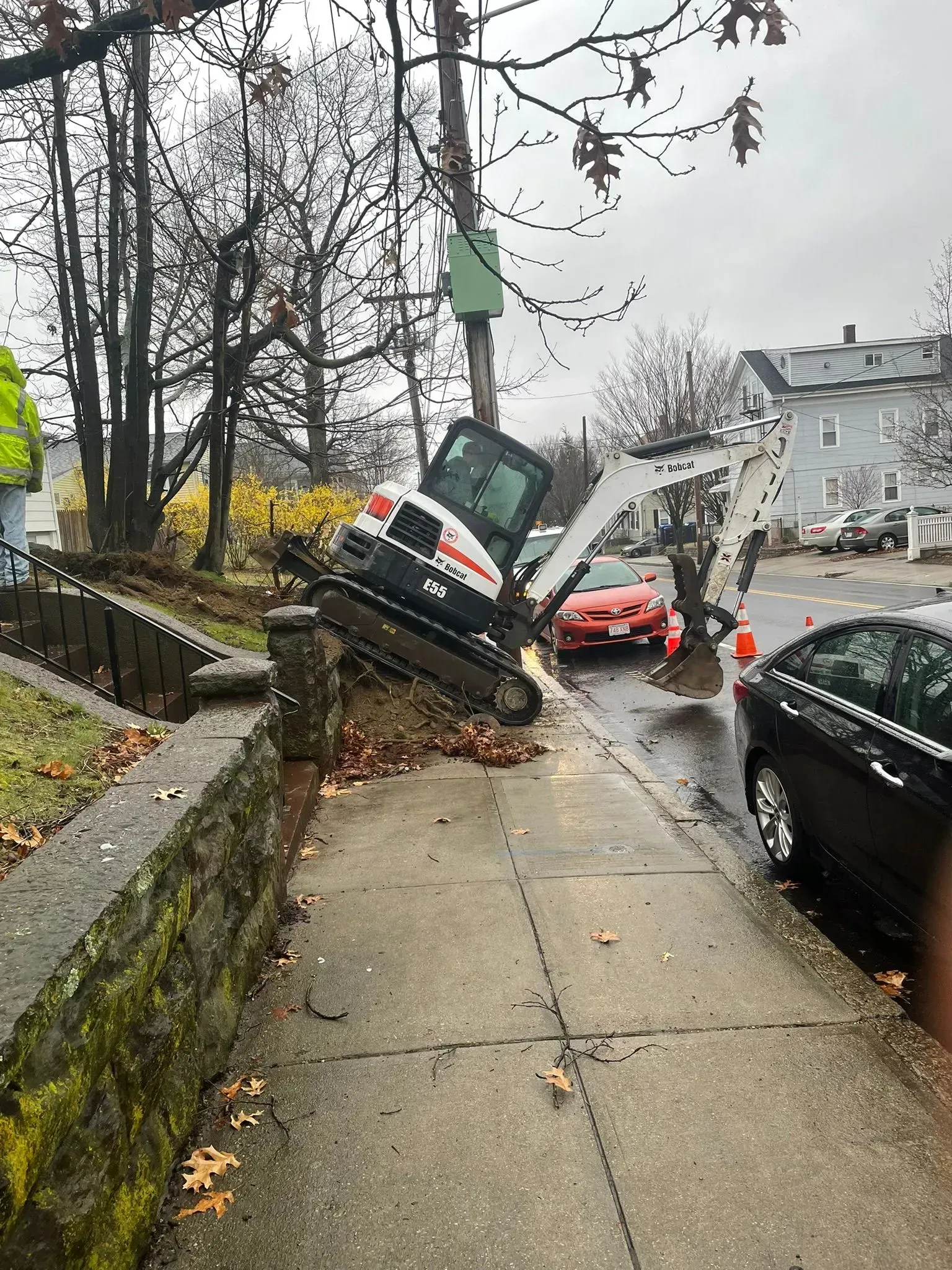 Car crashed onto a sidewalk, nose-up against a utility pole beside parked cars on a wet street.