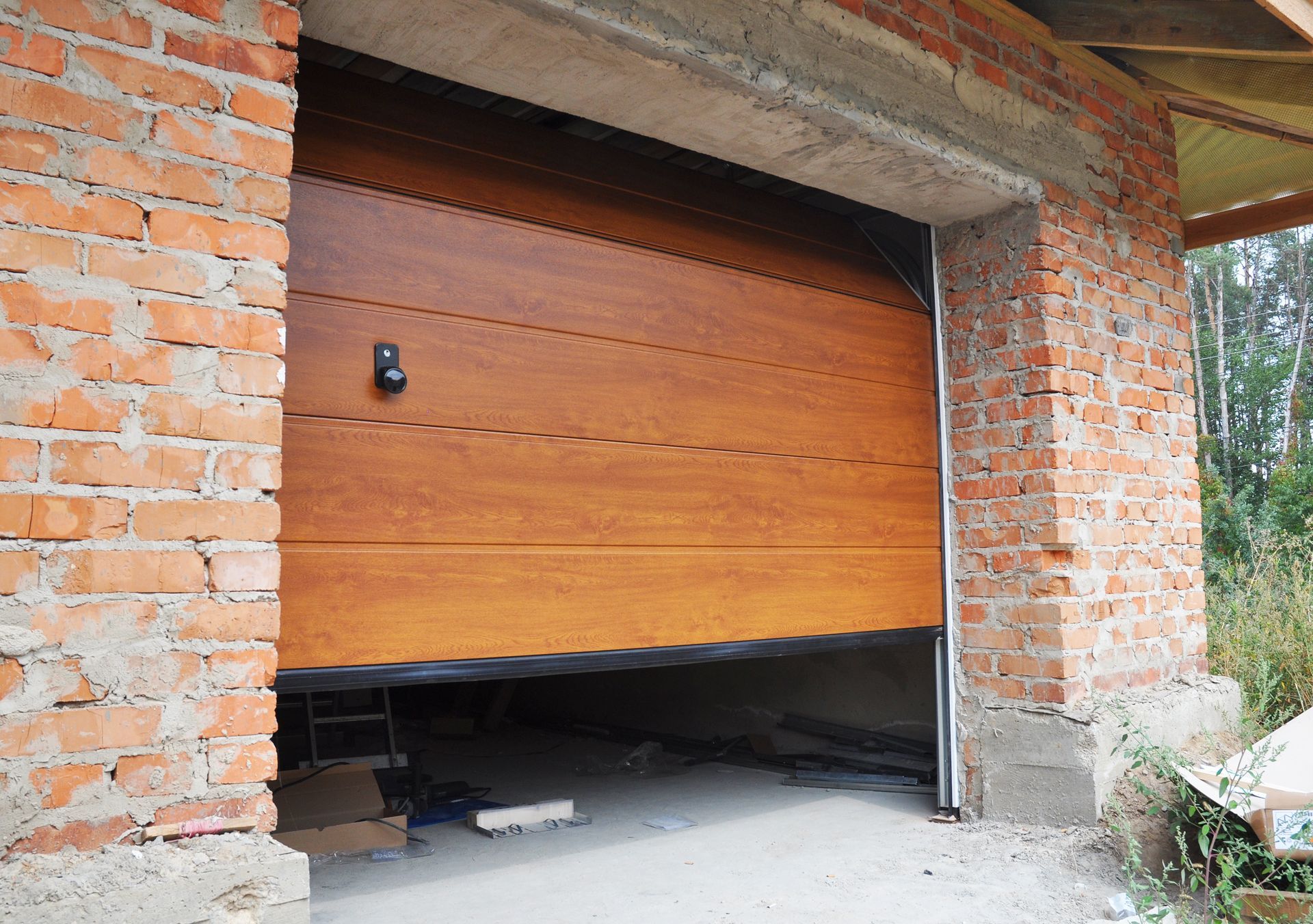 Partially open wooden garage door in a brick building, revealing the dark interior inside.