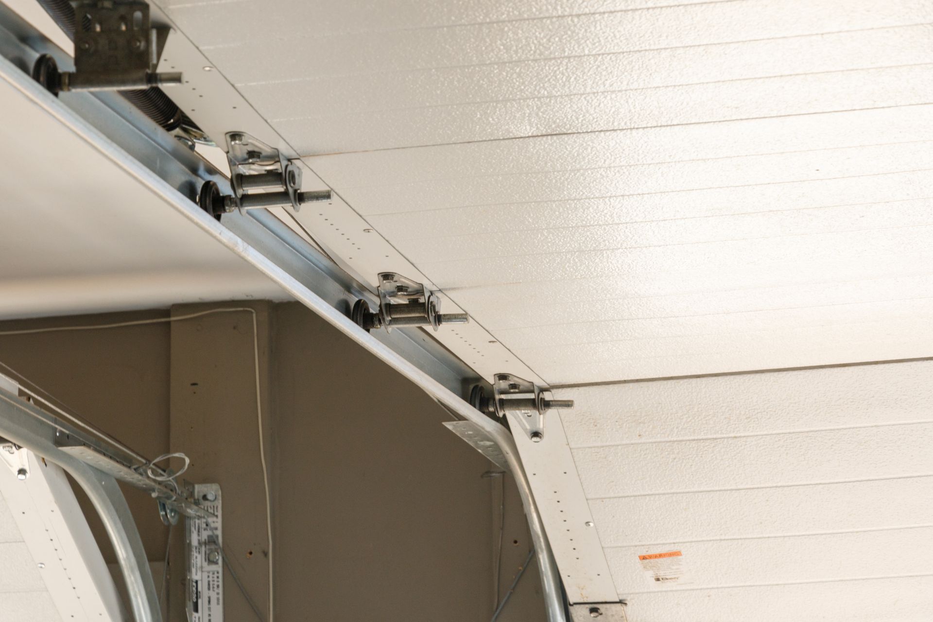 Open garage door track and hardware on a white ceiling panel.