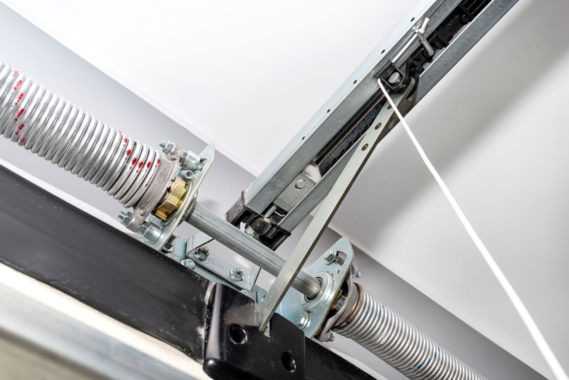 Close-up of a garage door spring and metal track mechanism on a white ceiling