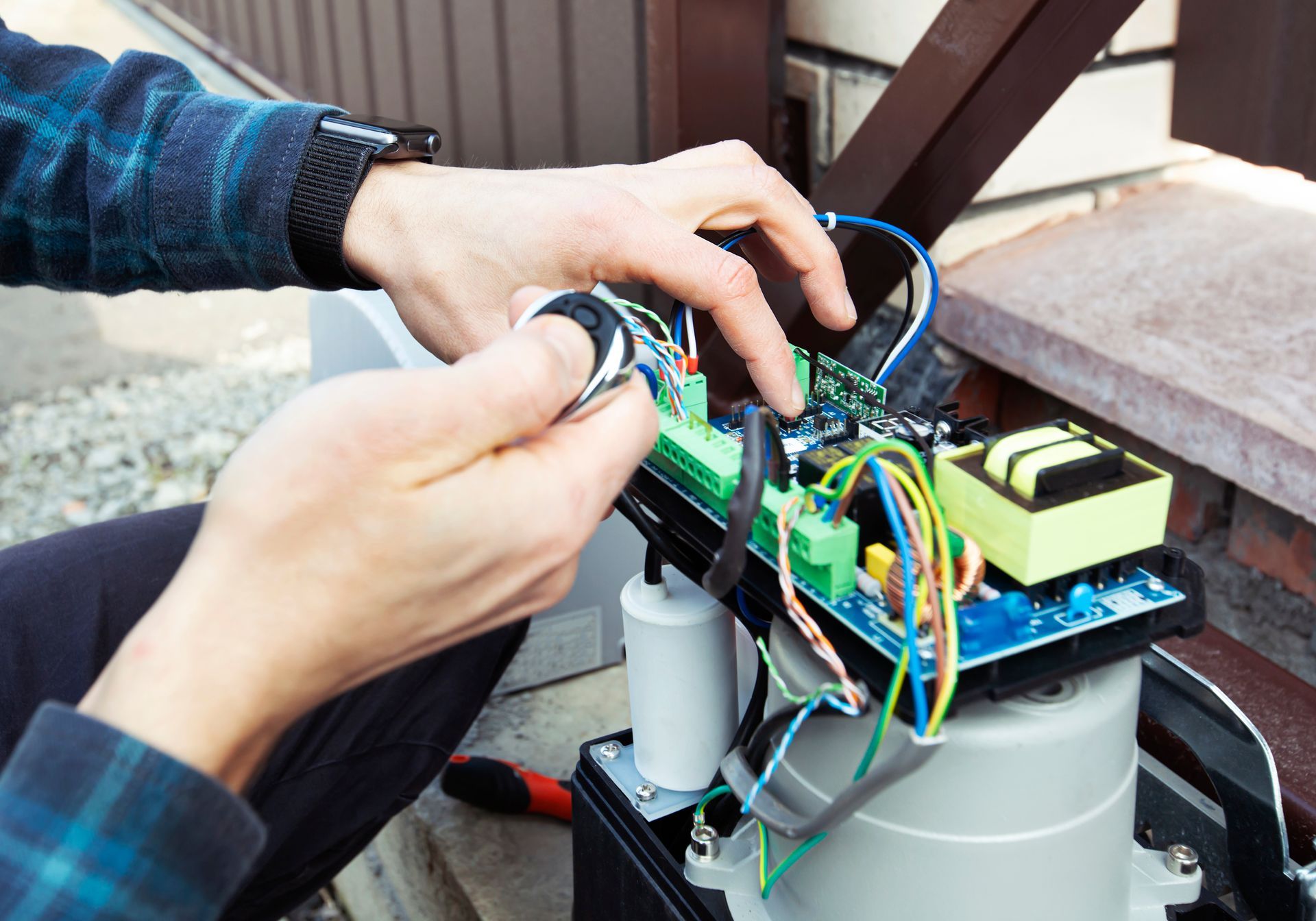 Hands wiring a small green circuit board on a robot or electronics device outdoors.