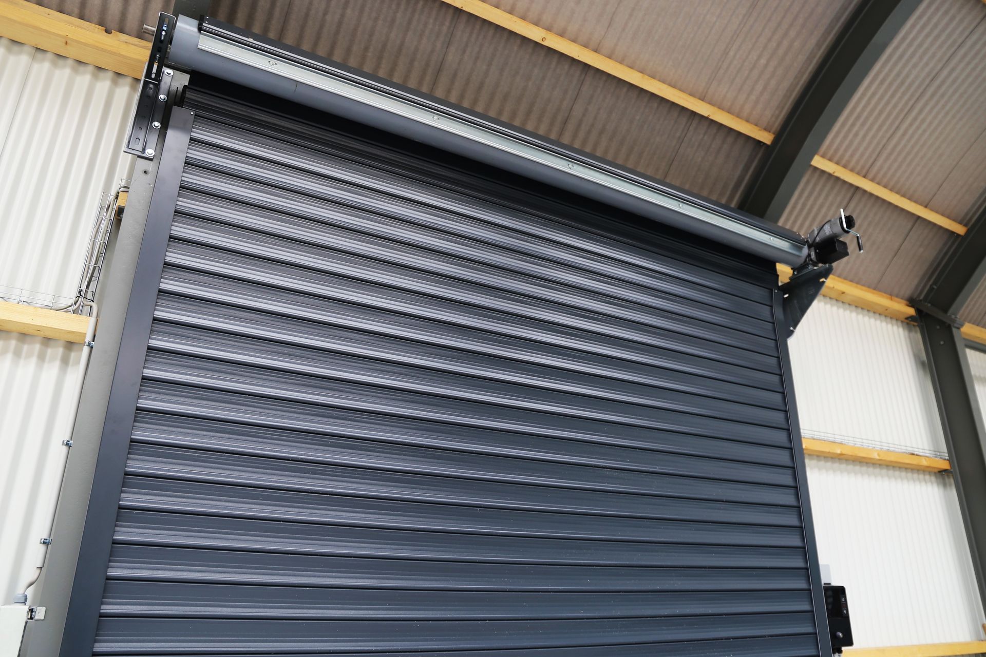 Large dark gray metal roll-up garage door inside an industrial warehouse.