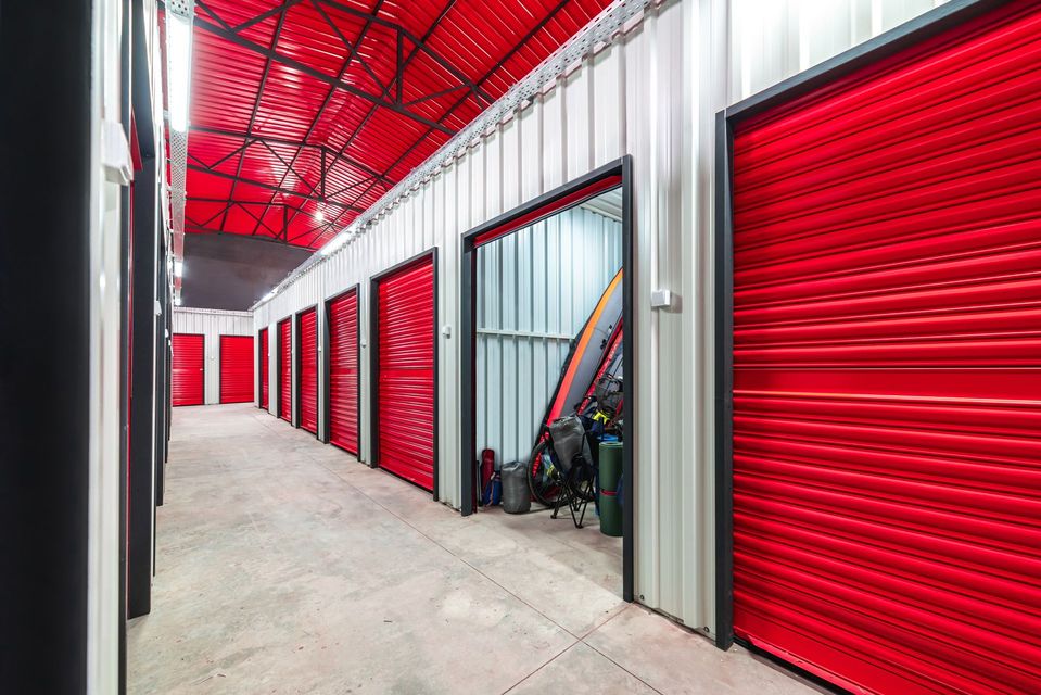 Storage facility hallway with red roll-up doors and a red ceiling, viewed from inside