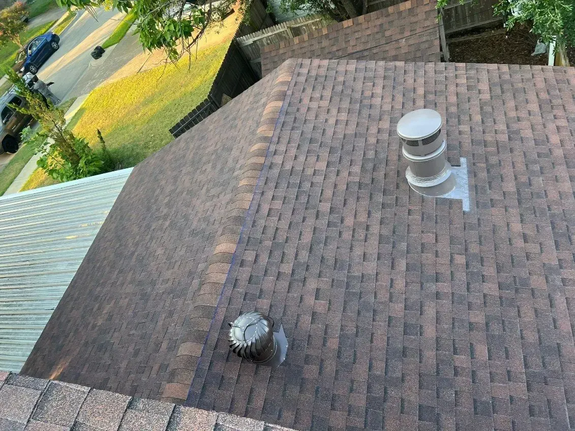 Overhead view of a brown shingled roof with a vent and a small chimney.