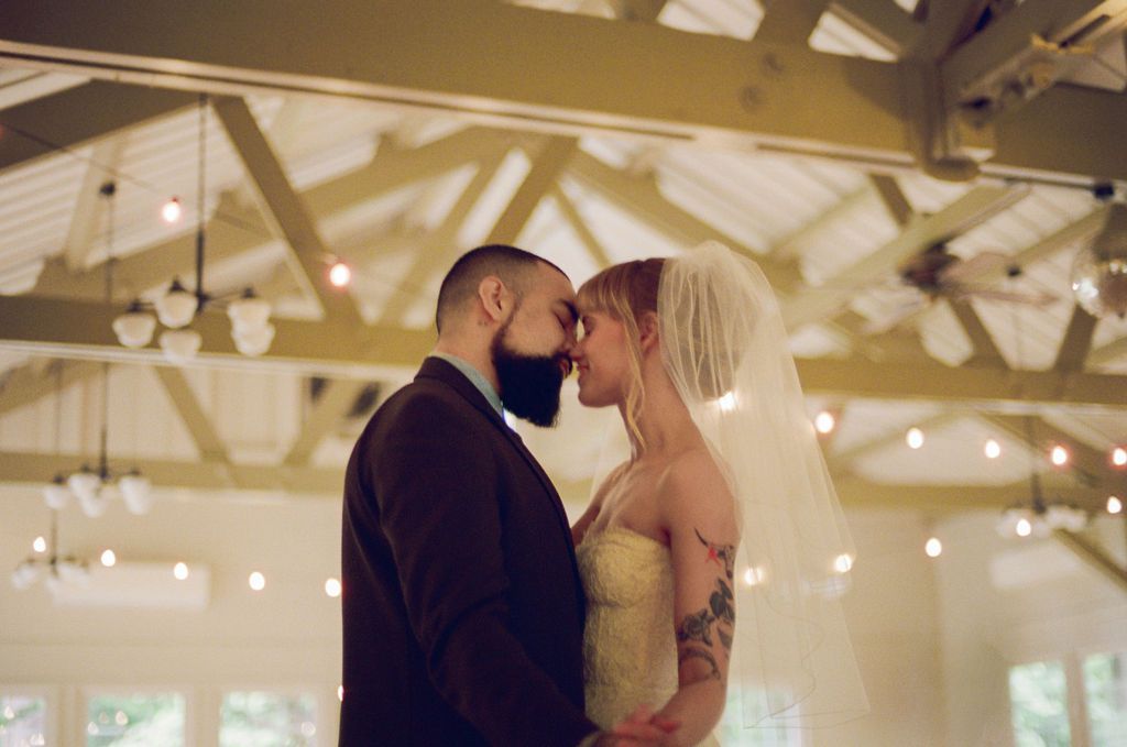 Bride and groom kissing in front of greenhouse with beautiful bouquet. 