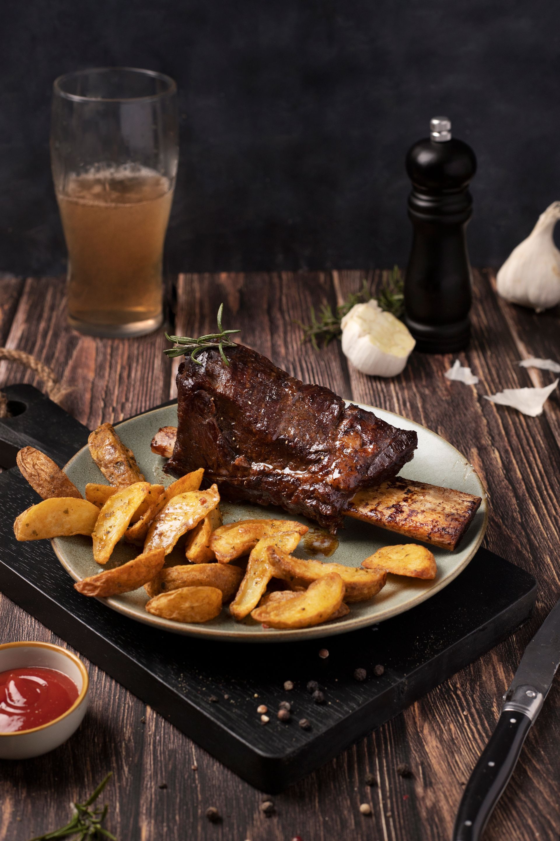Costillas de ternera servidas en un plato con patatas, cerveza y salsa, en un ambiente de asador y cervecería