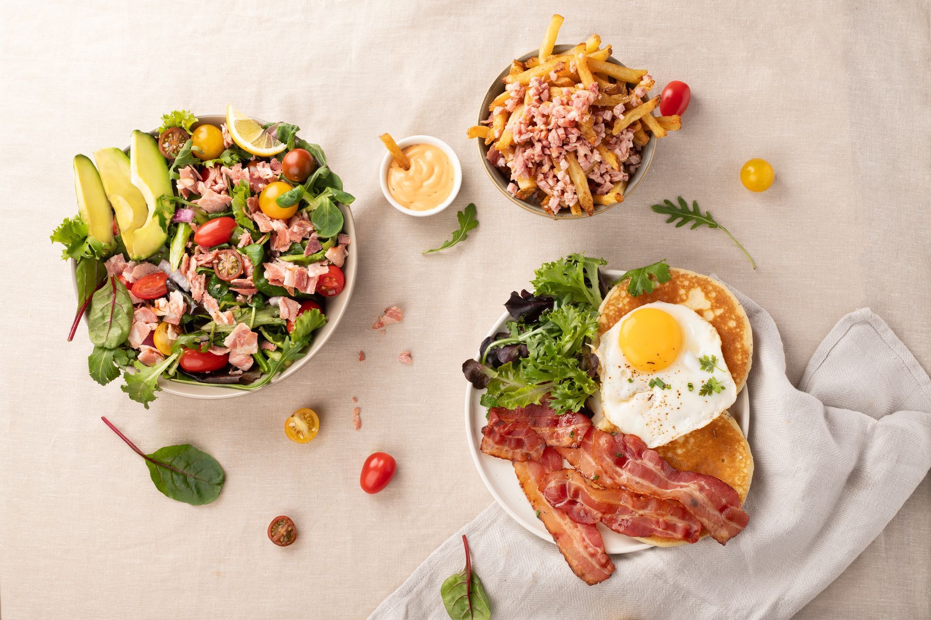 Une table garnie d'assiettes de nourriture comprenant une salade, des crêpes, du bacon et des œufs.
