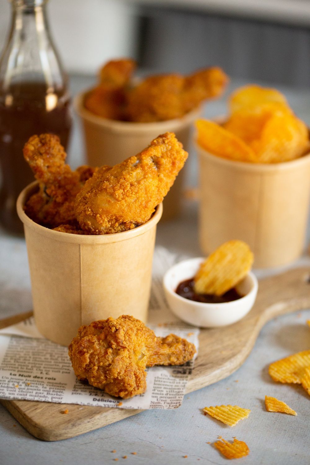Poulet frit et chips de pommes de terre dans des gobelets en papier sur une planche à découper en bois.