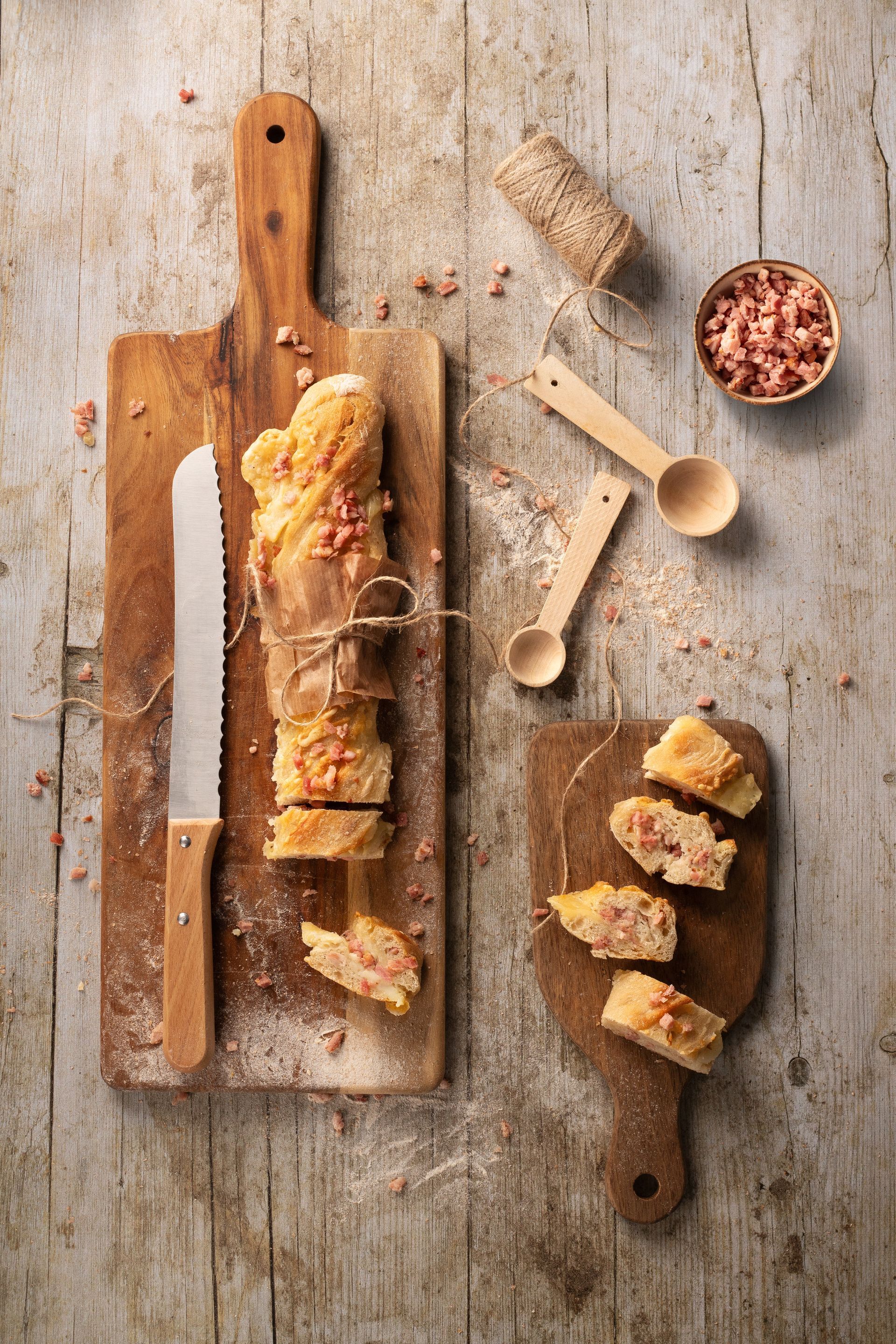 Baguette de pan para aperitivos con trocitos de beicon crujiente sobre una tabla de madera y un cuchillo.