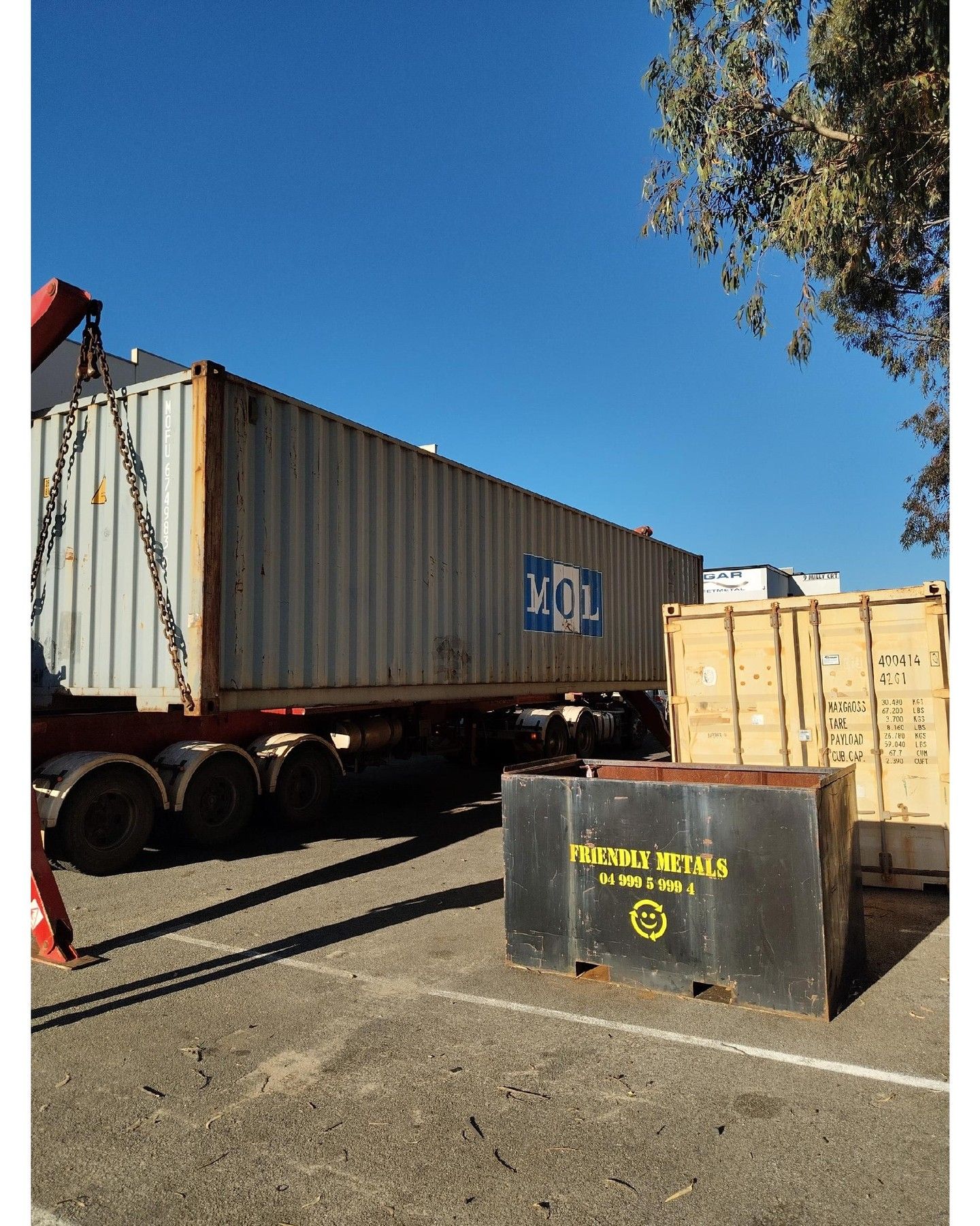 Shipping containers on a trailer under a blue sky, with other containers and a dumpster nearby.