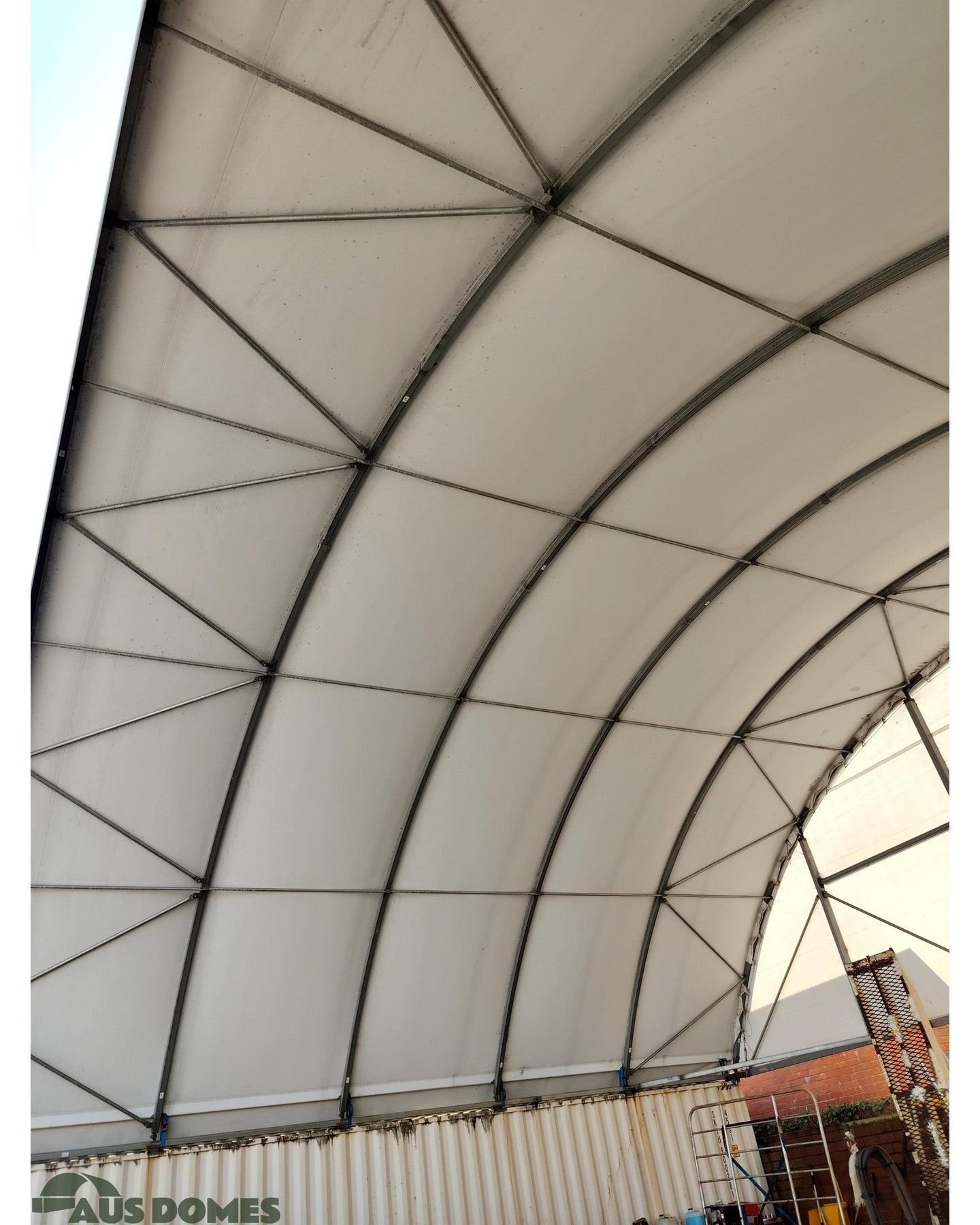 Interior view of a white, arched roof structure with steel beams and diagonal bracing, built on a container base.