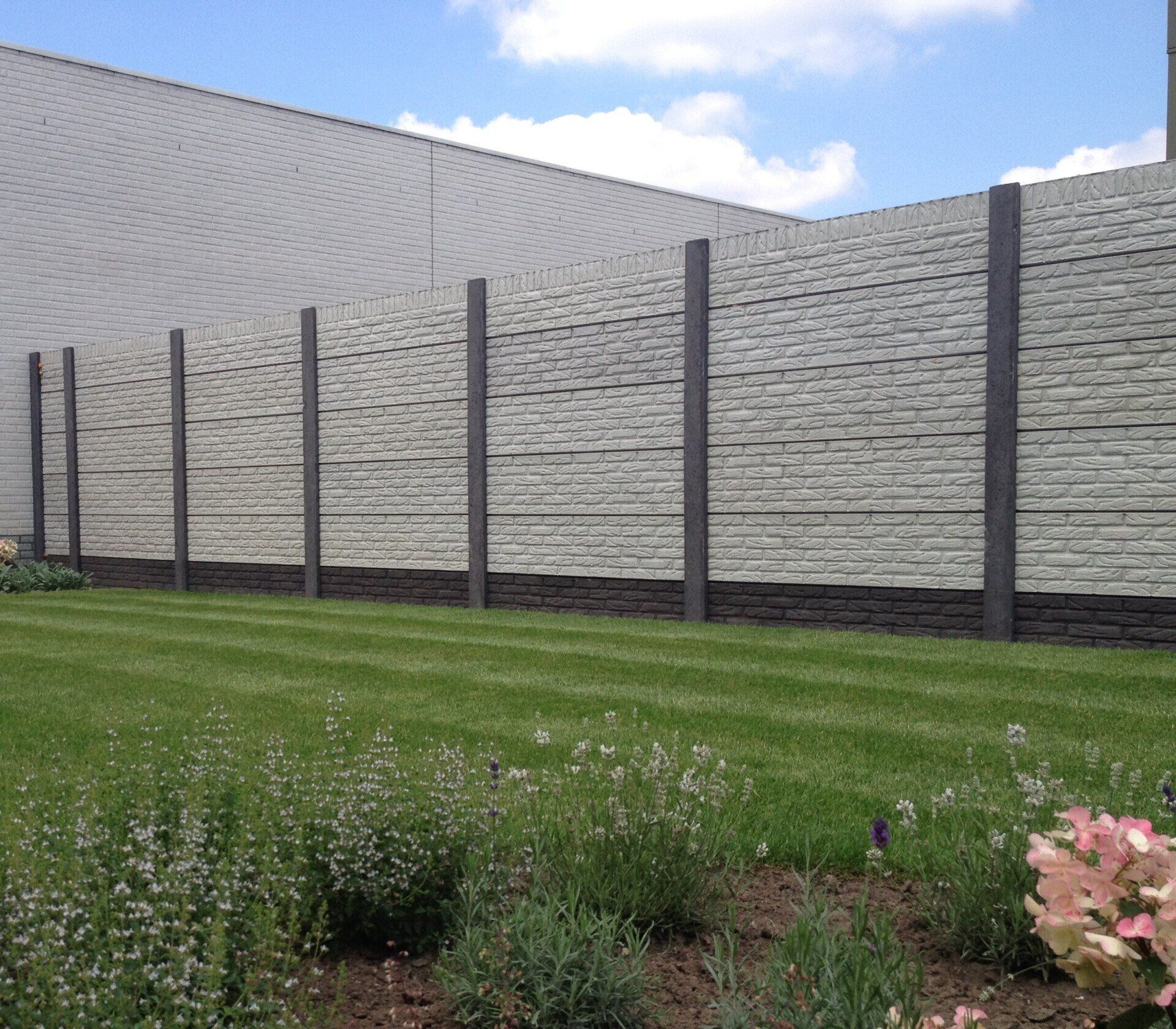 Lange betonnen schutting met grijze panelen en palen, geplaatst door A&B Betonbouw.