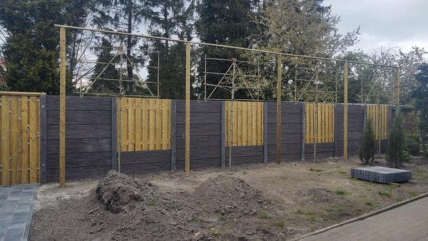 Houten schutting met betonnen onderplaten en gele panelen, erfafscheiding van A&B Betonbouw.