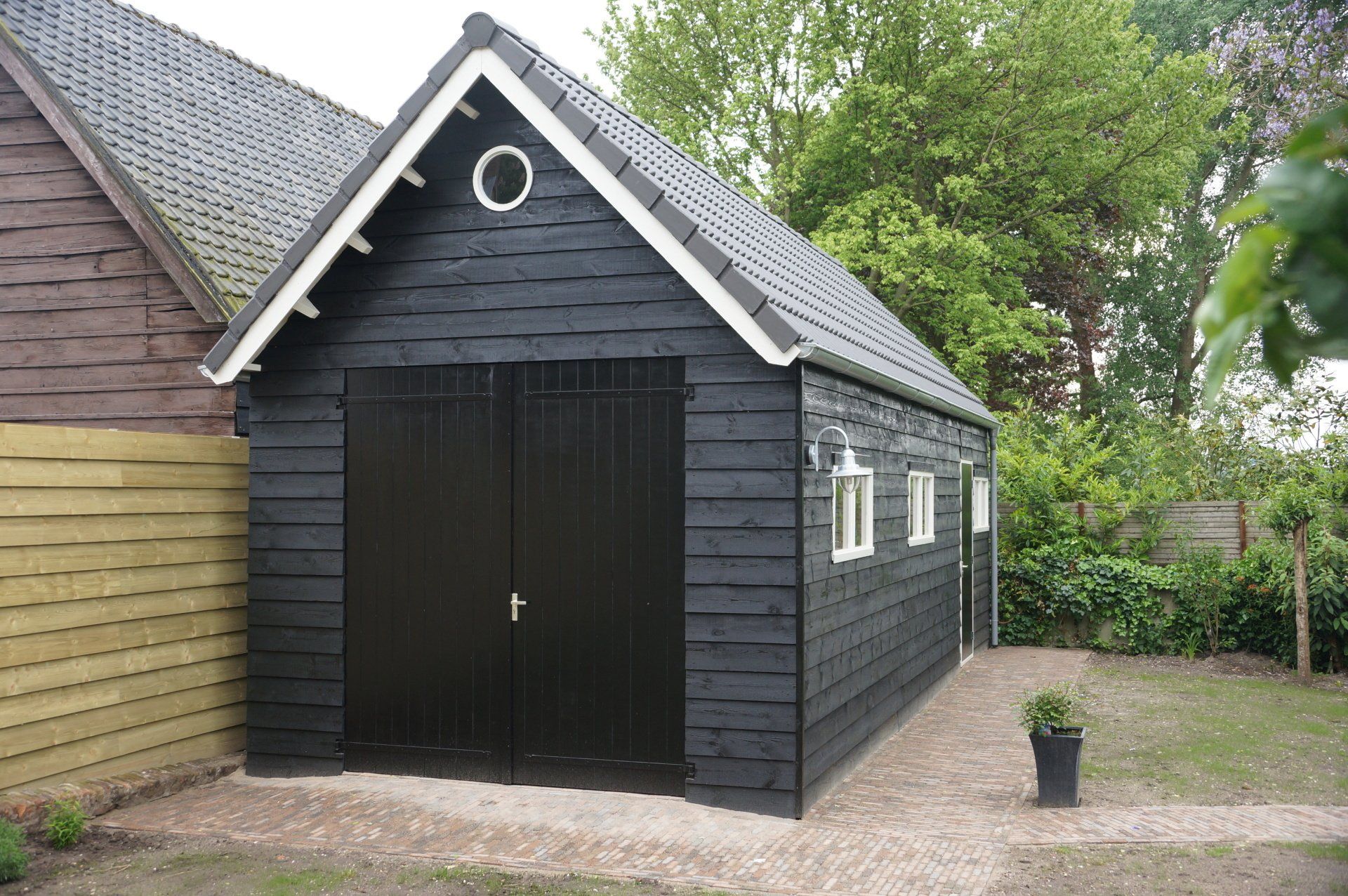 Zwarte houten garage met potdekseldelen en zadeldak, nieuw model van A&B Betonbouw.