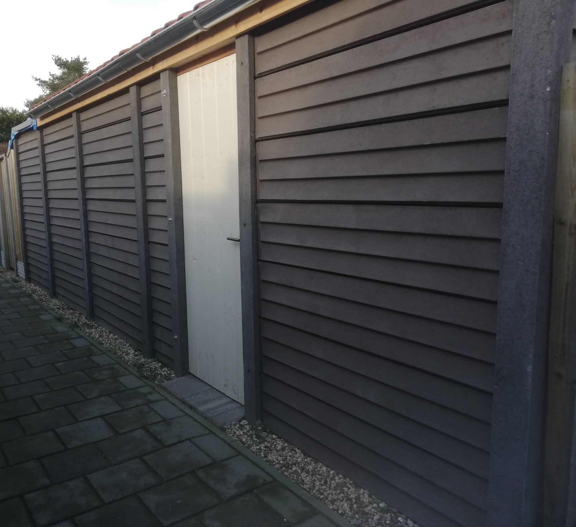 Houten schuur met donker rabatmotief en witte deur, gebouwd door A&B Betonbouw.