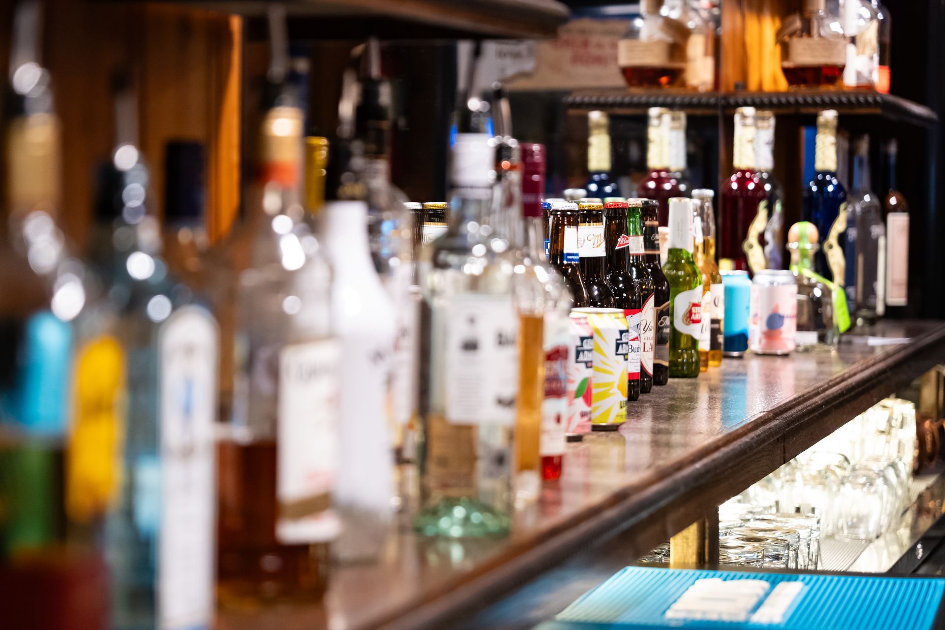 Bottles lined up on a wooden bar counter with shelves of liquor in the background