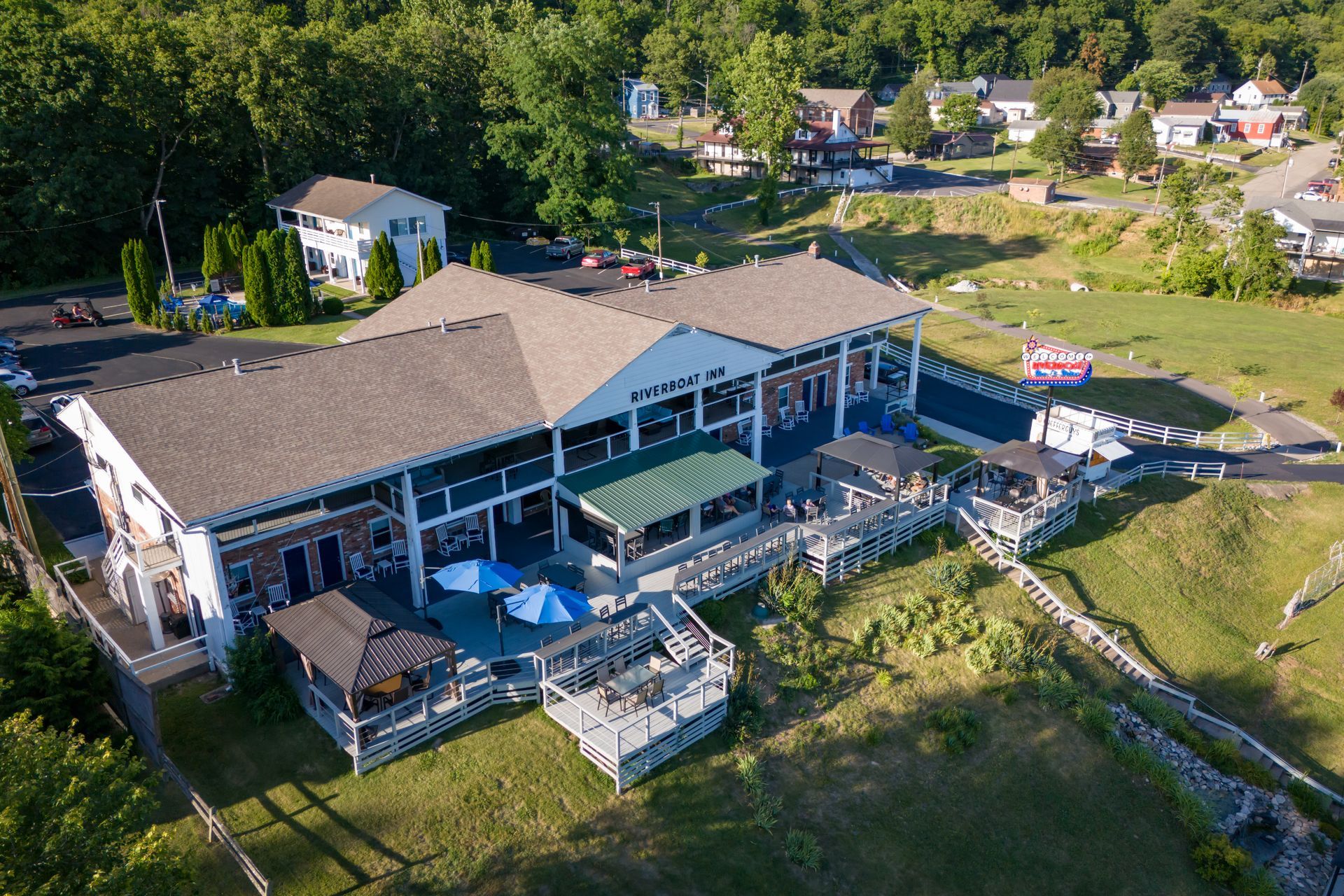 Aerial view of a  building with a deck, umbrellas, and grassy lawn 