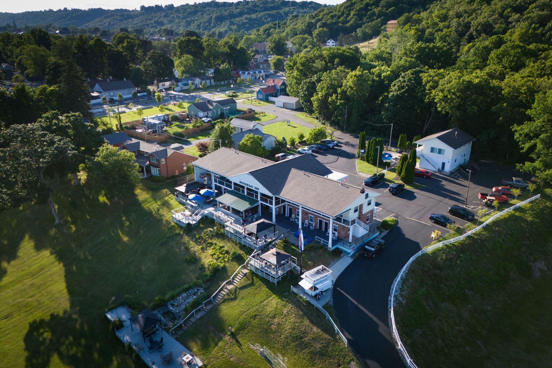 Aerial view of a white building and parked cars surrounded by trees in a rural area