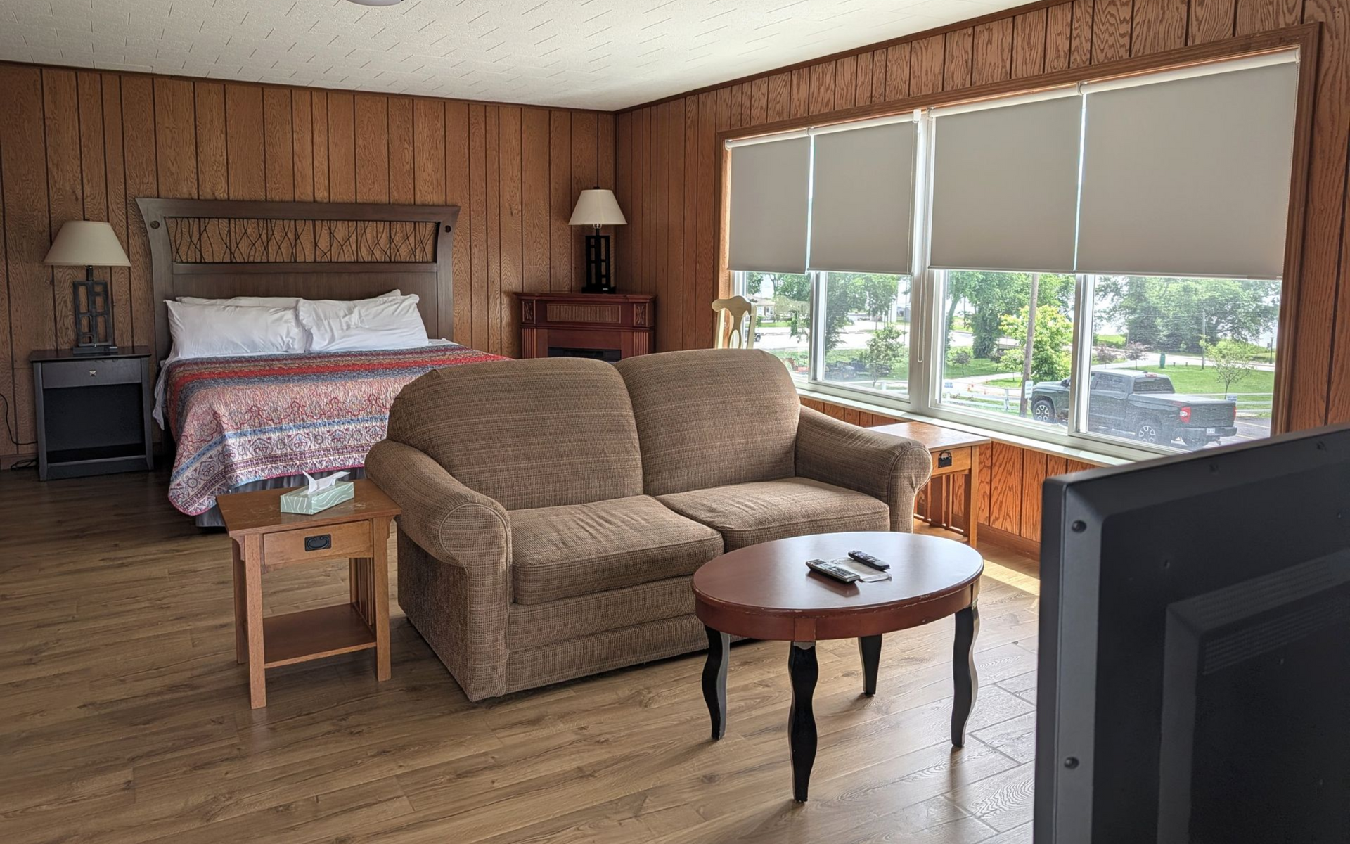 A cozy hotel room with a bed, sofa, small table, and large window overlooking water.