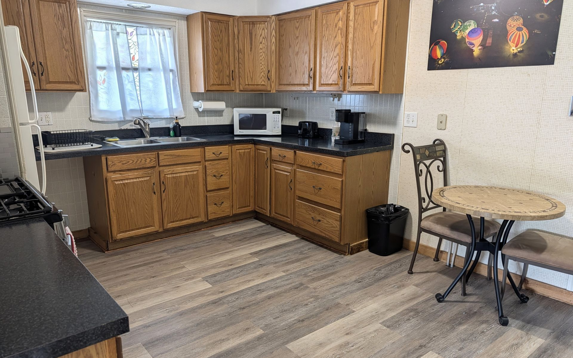 Small kitchen with wooden cabinets, black countertops, white appliances, and a round table with chairs.