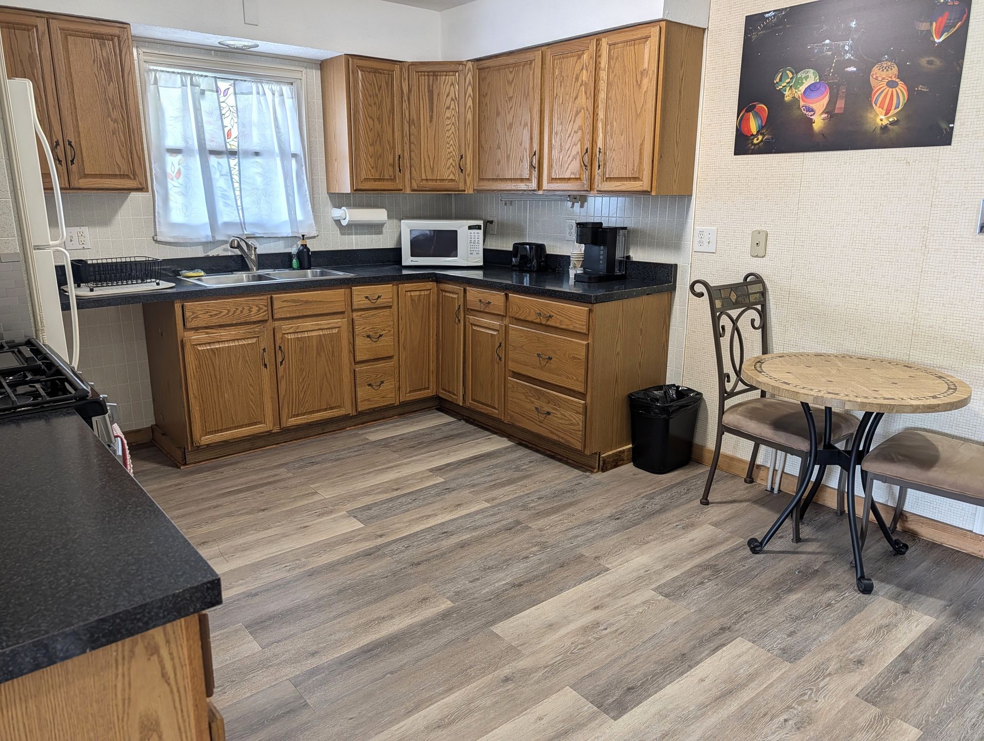 Small kitchen with wooden cabinets, black countertops, a microwave, and a round table by the wall.