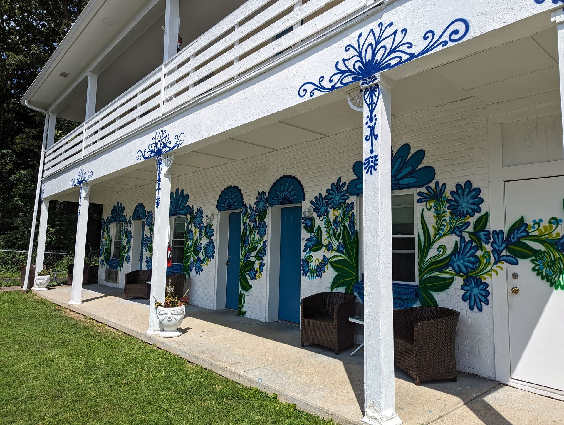 White building with blue floral murals, arched doorways, and white columns beside a grassy lawn.