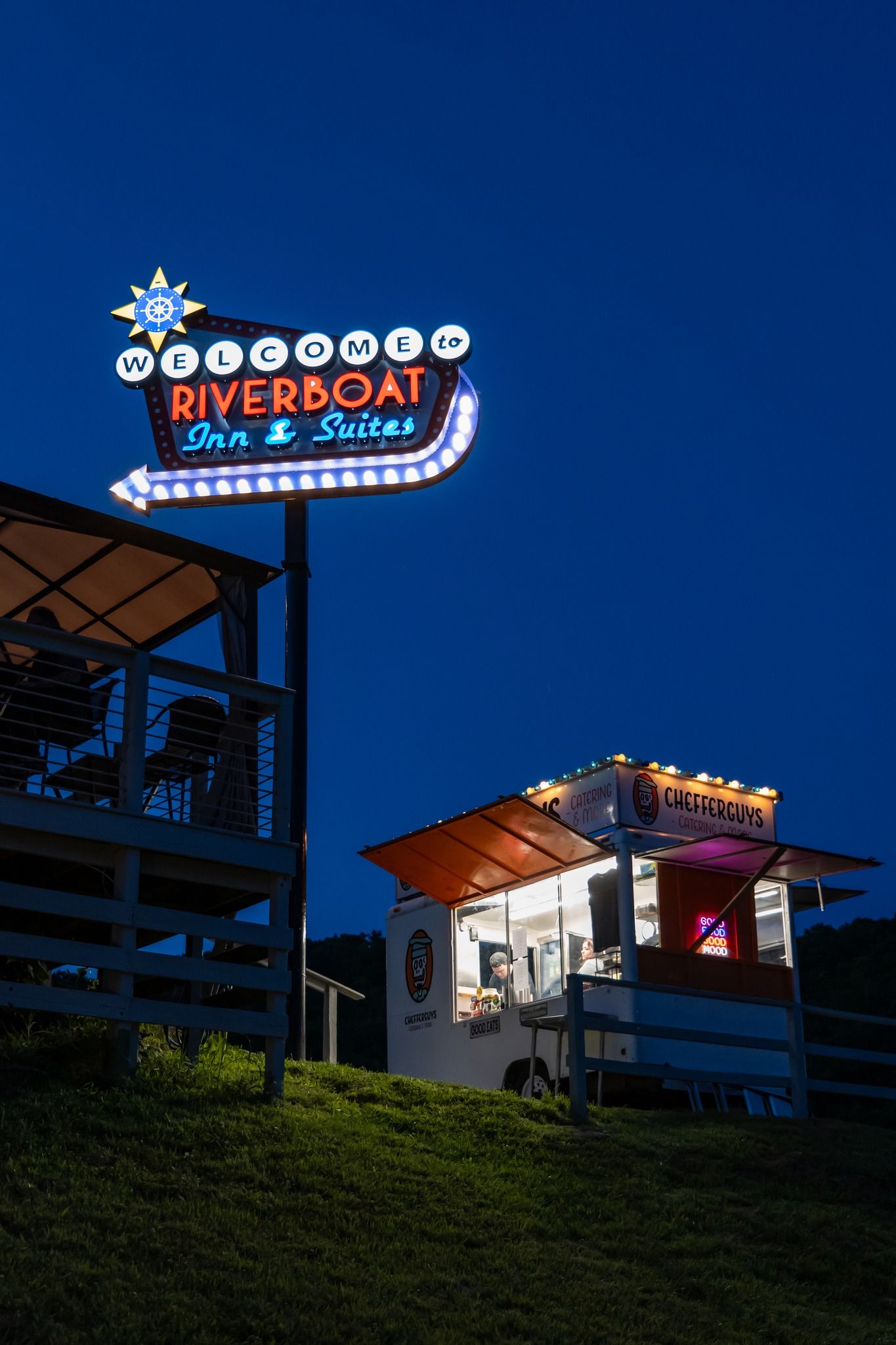 Neon Riverboat Inn & Suites sign above a lit deck at night on a hillside