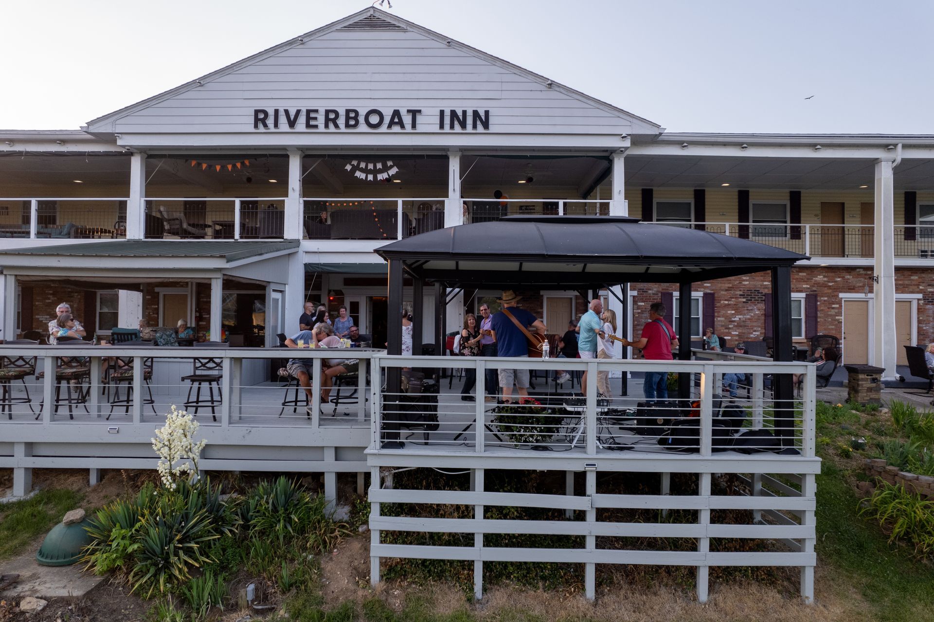 A group of people are standing on a deck in front of Riverboat Inn.