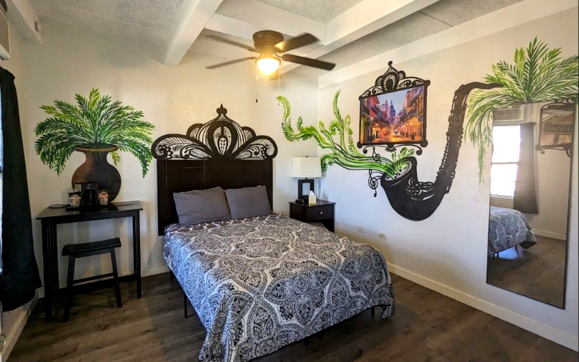 Elegant hotel room with dark carved bed, black side table, ceiling fan, mirror, and tropical plant décor