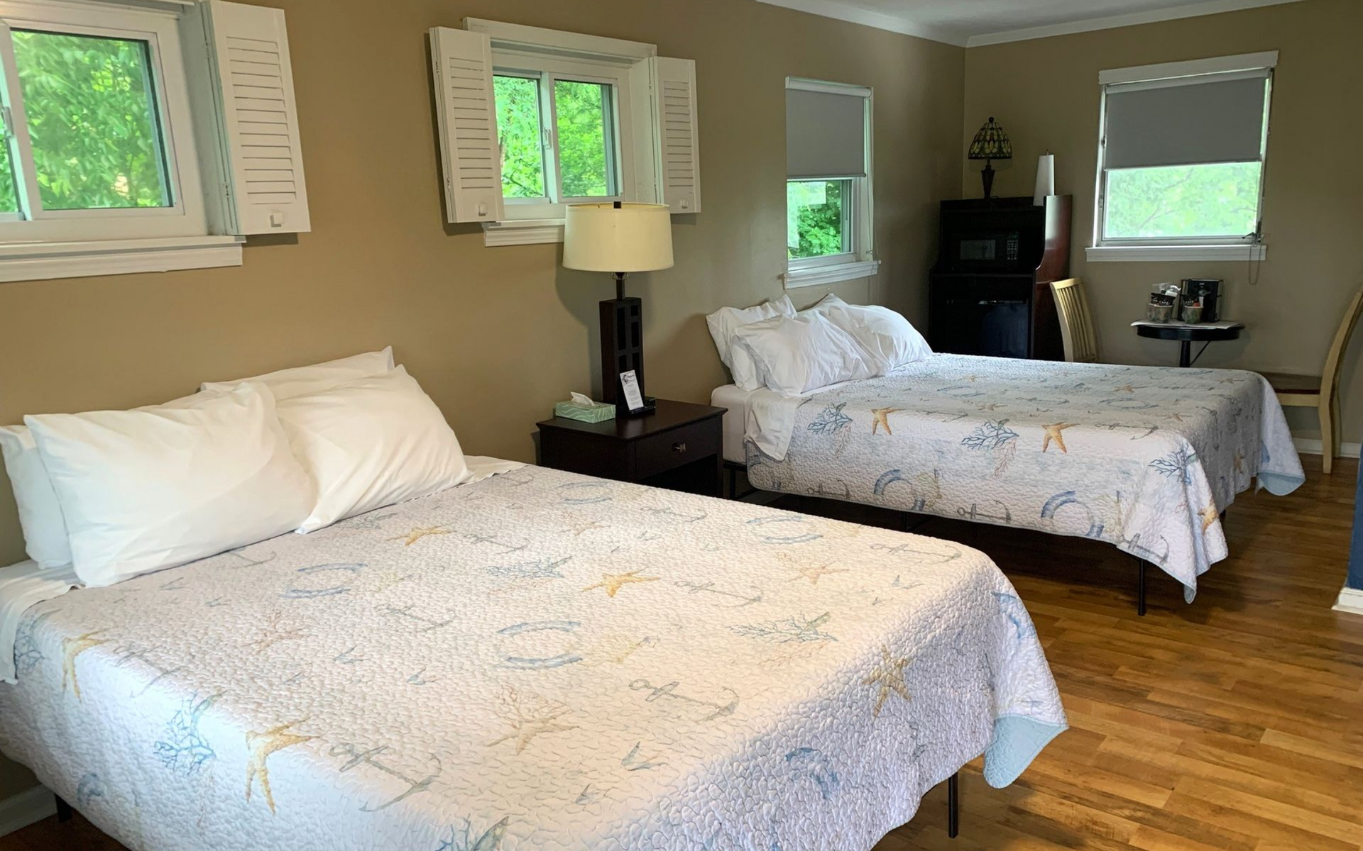 Bright hotel room with two white beds, beige walls, wood floor, and windows with blinds