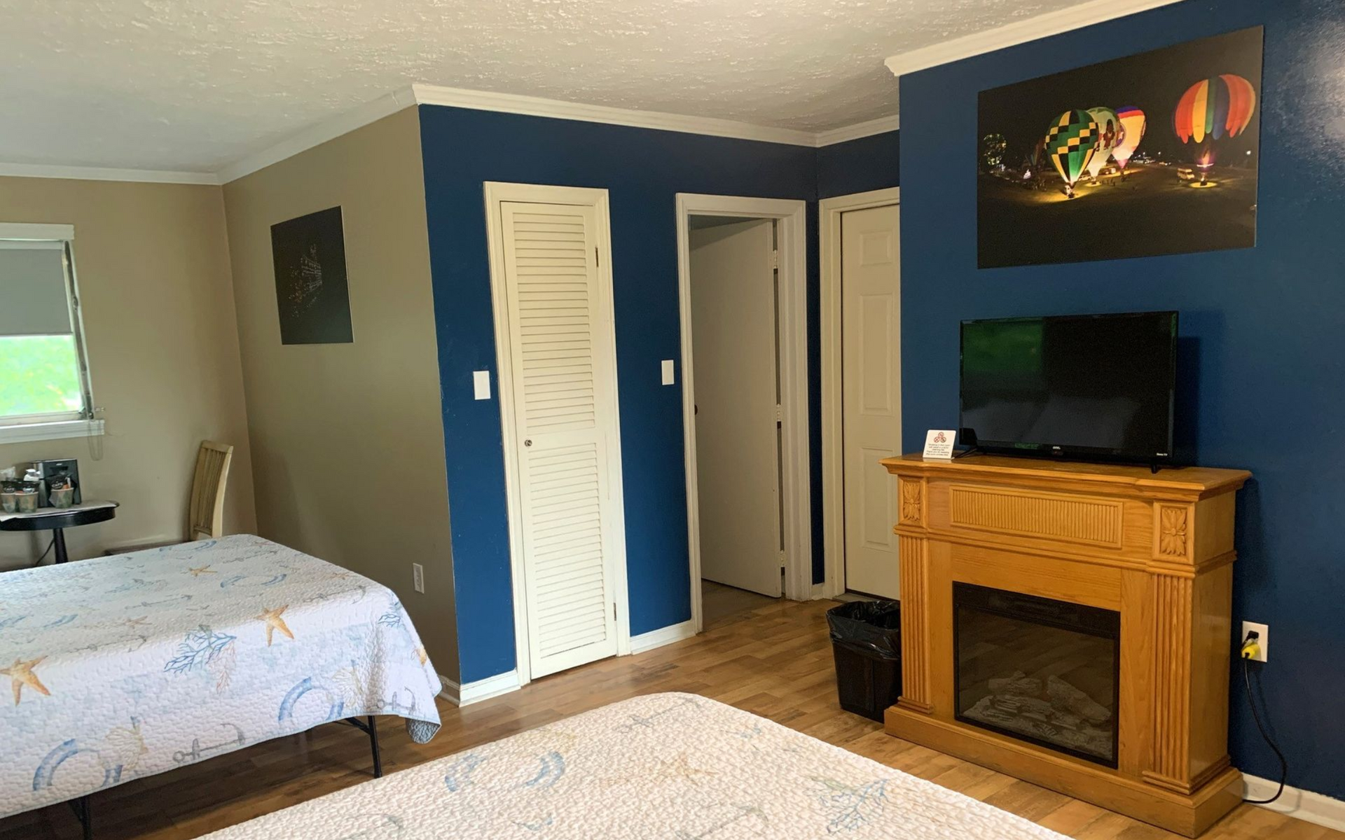 Hotel room with blue accent wall, bed, TV, and wooden fireplace mantel