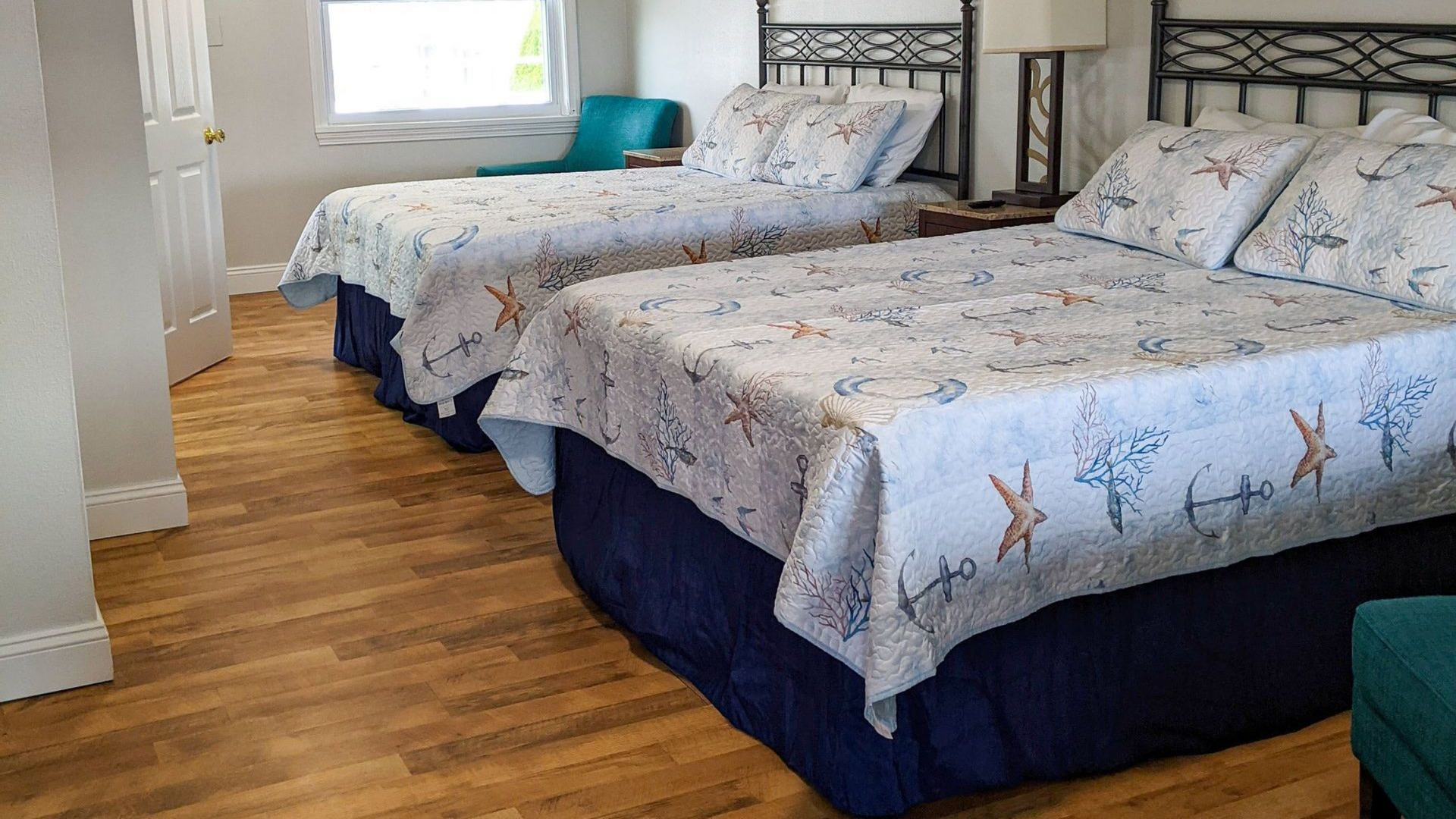 Hotel room with two twin beds, blue bed skirts, and hardwood floor near a window.
