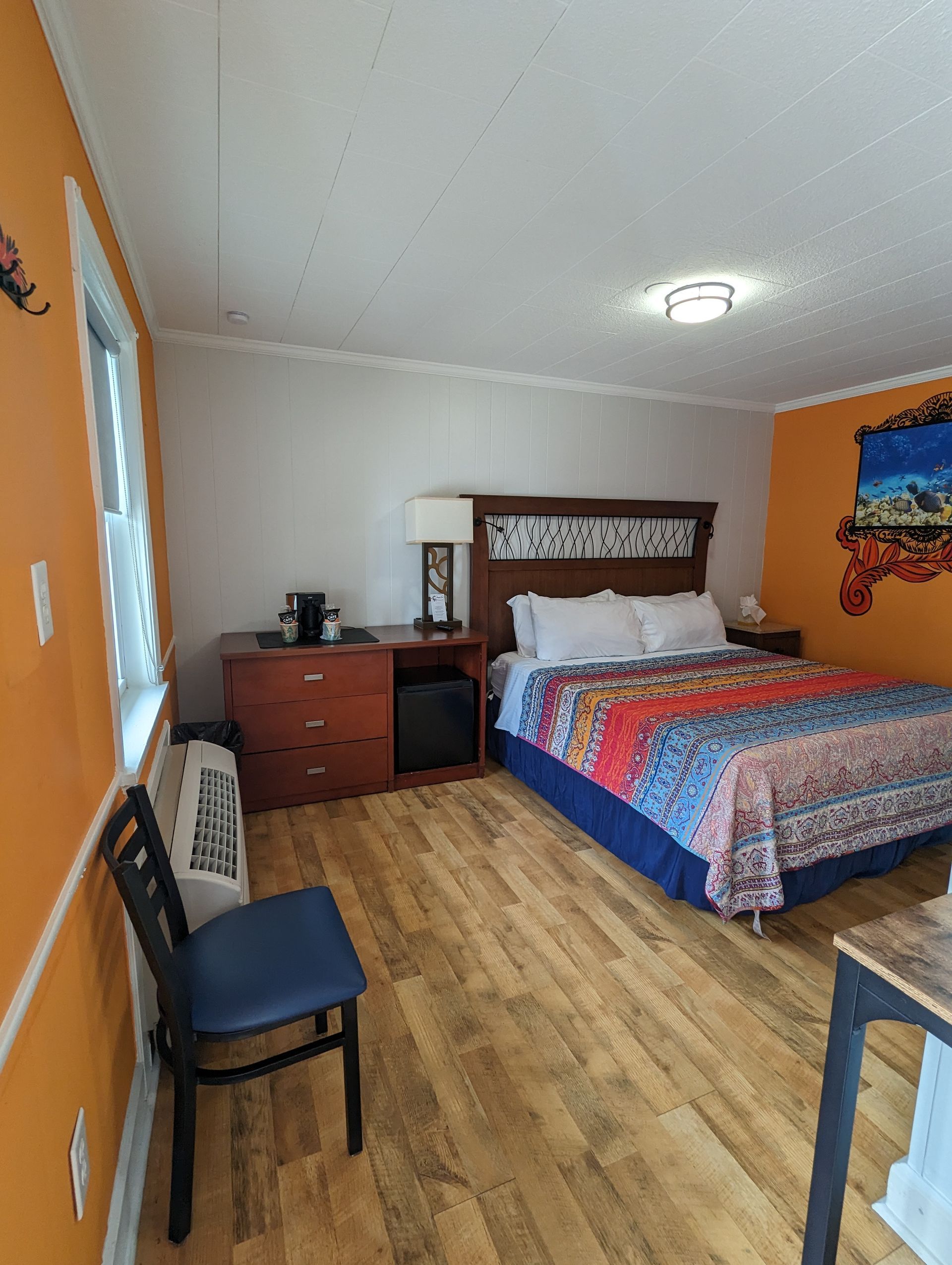 Bedroom with orange walls, wood floor, bed, dresser, chair, and nightstand.