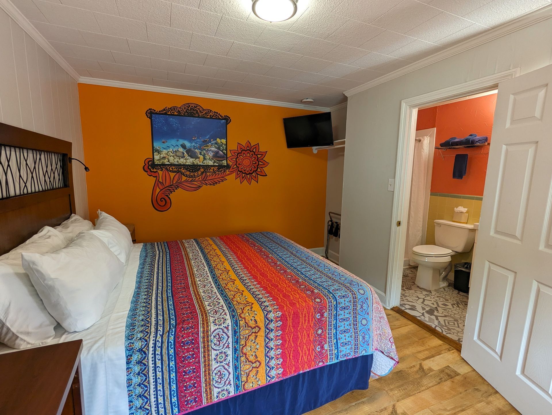 Colorful bedroom with orange accent wall, bed, and open door to a small bathroom