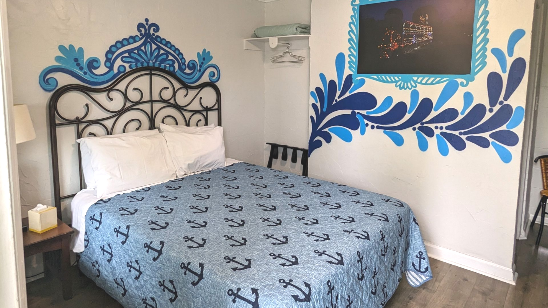 Hotel room with ornate black headboard, blue floral wall art, and blue patterned bedspread.