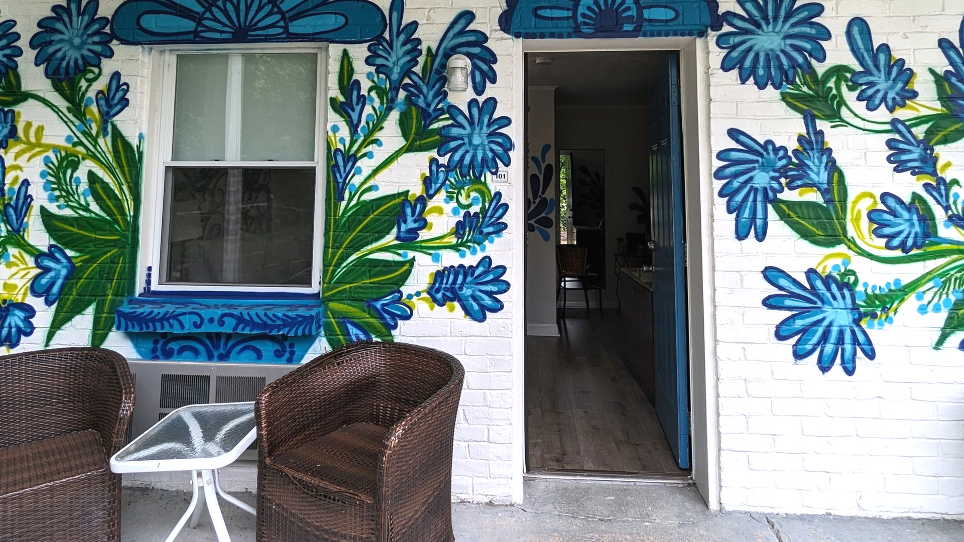 Patio with blue floral wall mural, two chairs, and an open doorway into a hotel room