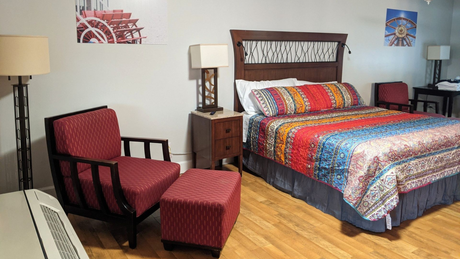 Hotel room with king  bed, red chair and ottoman, lamps, and colorful quilt on wood floor