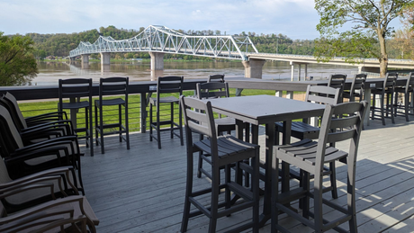 Outdoor patio seating with black tables and chairs overlooking the Ohio river and a steel bridge
