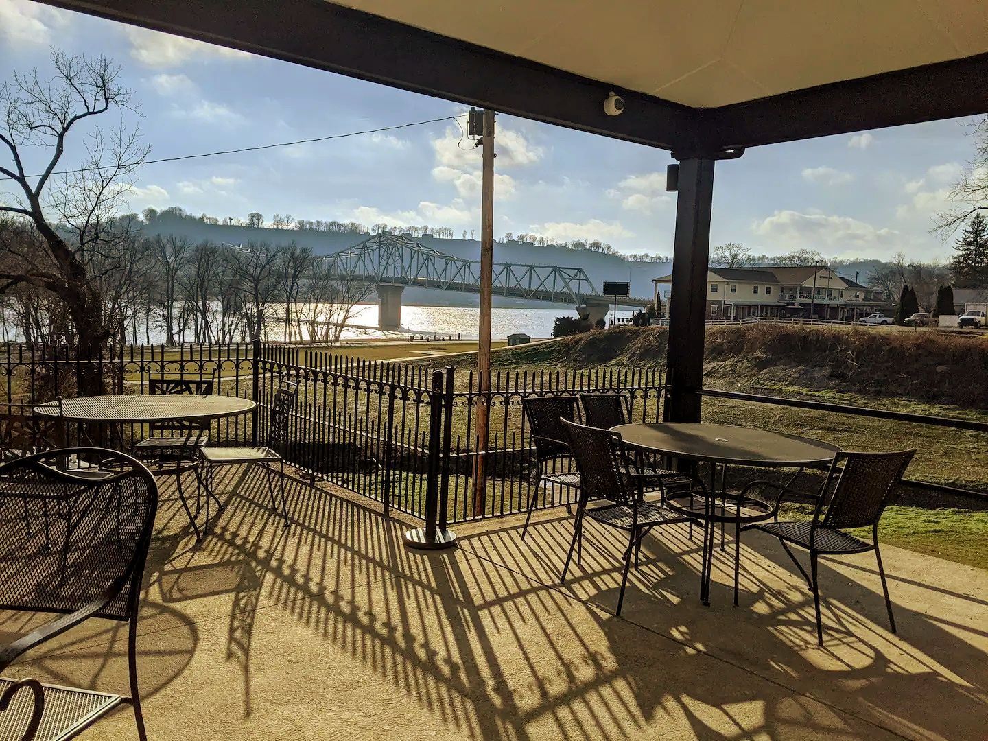 A patio with tables and chairs overlooking a river and a bridge.