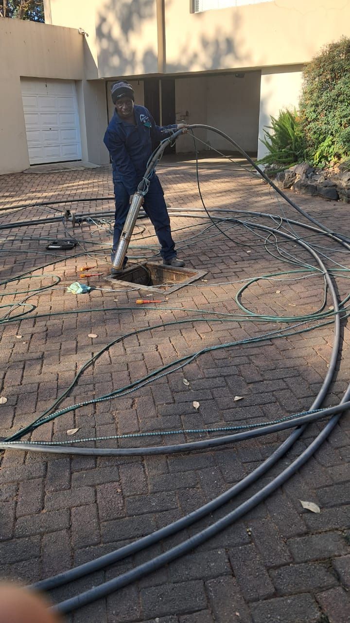 A man is using a hose to clean a drain in a driveway.