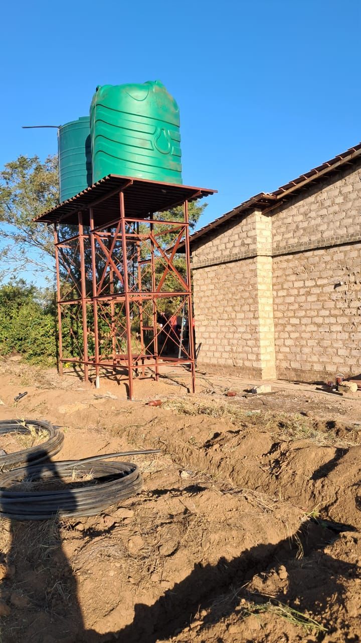 A water tower is sitting in the dirt in front of a brick building.