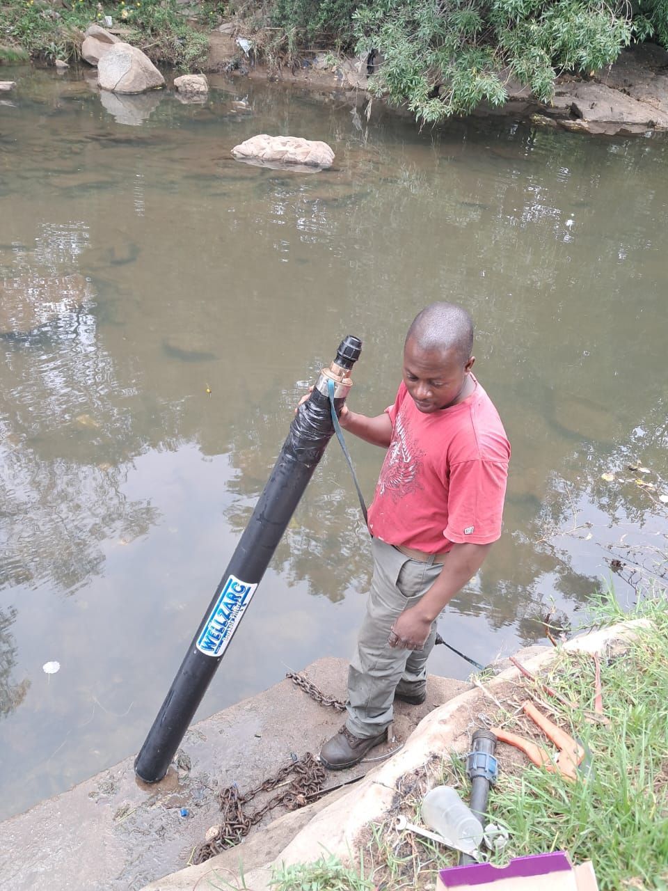 A man is standing next to a river holding a large pipe.