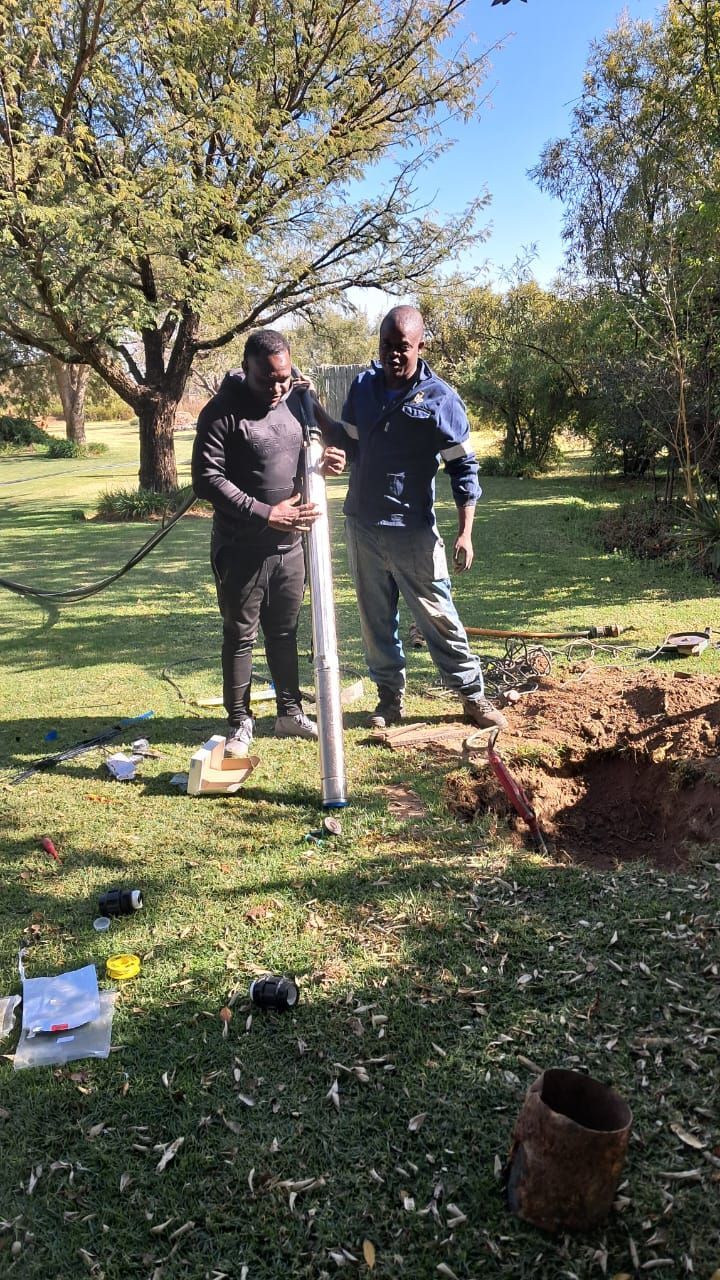 Two men are working on a water pump in a field.