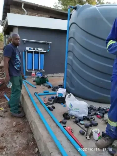 A man is standing next to a water tank while another man works on it.