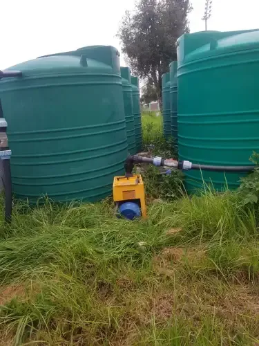 A row of green water tanks are sitting in a grassy field.