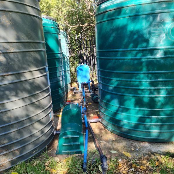 A man in a blue shirt is standing in front of a row of green water tanks.