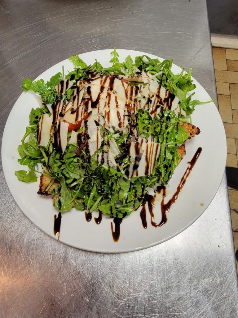 Salad on a white plate with dark balsamic drizzle, served on a metal countertop